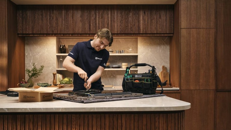 Tecnico dell’assistenza che ripara un piano cottura in una cucina con pannelli in legno